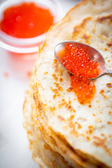 A stack of thin russian pancakes with caviar on a white plate