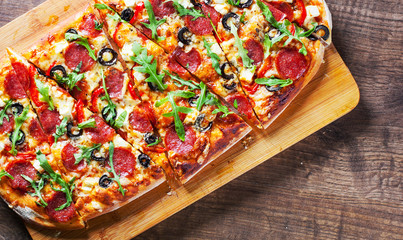 Pizza with Mozzarella cheese, salami, pepper, pepperoni, olives, Spices and Fresh arugula. Italian pizza on wooden table background