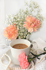 A cup of coffee and flowers on a light background, wishes of good morning and good day, a cozy home