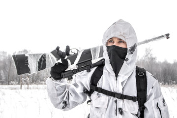 Man soldier in the winter on a hunt with a sniper rifle in white winter camouflage goes to the field