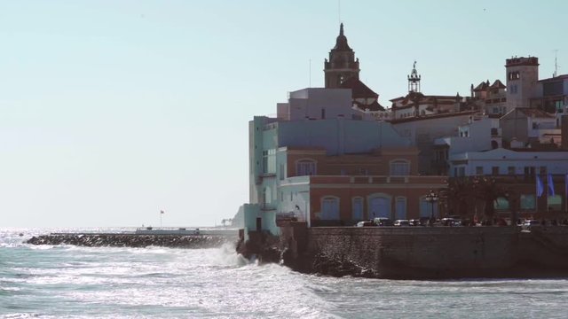 Slowmotion waves crashing in mediterranean town of Sitges, with the iconic Church of Santa Tecla in Barcelona province, Spain.