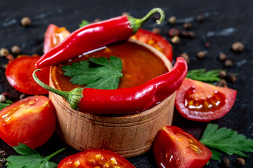 Ketchup with fresh cherry tomatoes, chili Pepper, spices and herbs on black stone background. The concept of cooking, ingredients