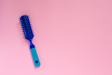 Blue plastic hair for combing hair on pink background with copyspace. - obrazy, fototapety, plakaty