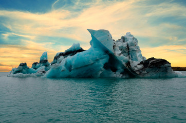 Large jagged iceberg in Glacier Lagoon Lake in Iceland with sunset behind it. 
