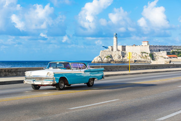 Amerikanischer blau weisser Cabriolet Oldtimer auf dem berühmten Malecon und im Hintergrund die Festung Castillo de los Tres Reyes del Morro in Havanna Kuba - Serie Kuba Reportage
