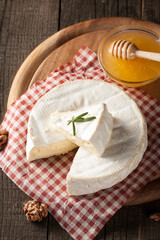 Brie type of cheese. Camembert cheese. Fresh Brie cheese and a slice on a wooden board with nuts, honey and leaves. Italian, French cheese.