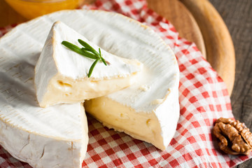 Brie type of cheese. Camembert cheese. Fresh Brie cheese and a slice on a wooden board with nuts, honey and leaves. Italian, French cheese.