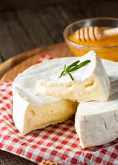 Brie type of cheese. Camembert cheese. Fresh Brie cheese and a slice on a wooden board with nuts, honey and leaves. Italian, French cheese.