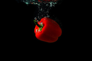 Red bell pepper falling in water with splash on black background, paprika, stop motion photography....