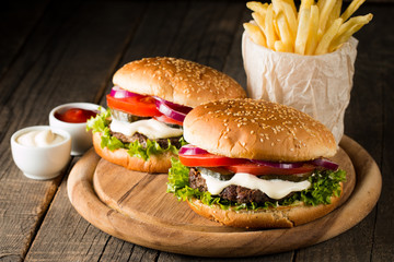 Close-up photo of home made hamburger with beer made of beef, onion, tomato, lettuce, cheese and spices. Fresh burger closeup on wooden rustic table with potato fries and chips.