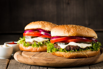 Close-up photo of home made hamburger with beer made of beef, onion, tomato, lettuce, cheese and spices. Fresh burger closeup on wooden rustic table with potato fries and chips.