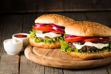 Close-up photo of home made hamburger with beer made of beef, onion, tomato, lettuce, cheese and spices. Fresh burger closeup on wooden rustic table with potato fries and chips.