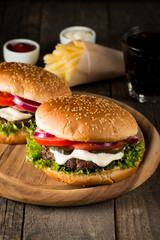 Close-up photo of home made hamburger with beer made of beef, onion, tomato, lettuce, cheese and spices. Fresh burger closeup on wooden rustic table with potato fries and chips.