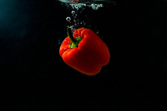 Red bell pepper falling in water with splash on black background, paprika, stop motion photography. Red pepper.