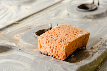 Orange sponge on background of a dirty gas stove.