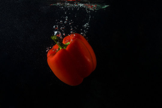 Red bell pepper falling in water with splash on black background, paprika, stop motion photography. Red pepper.