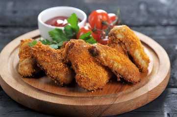 Chicken wings with crispy crust. The composition is complemented by cherry tomatoes, parsley and a chachka with ketchup sauce. Dark wooden background. Close-up. 