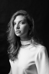 Black and white fashion portrait of beautiful model woman with luxurious curly hair in elegant white blouse posing in studio in front of black background. Art photo portrait