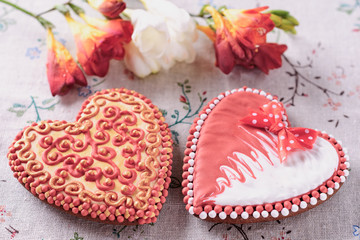 A pair of beautiful home-made gingerbreads for a wedding celebration or Valentine's day next to flowers on a table, closeup