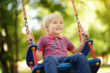 Cute little boy having fun on outdoor playground. Child on swing