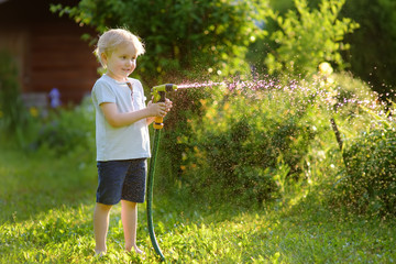 Funny little boy playing with garden hose in sunny backyard