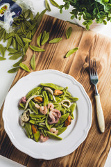 spinach pasta with seafood on a white plate on a wooden Board