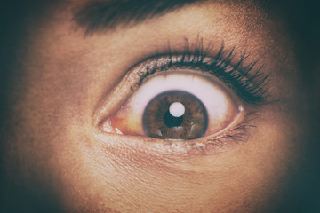Eye peeking through peep hole watching something scary. Scared woman with look of horror in her...