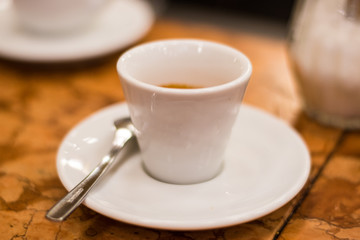 White Espresso Coffee Cup On A White Saucer With A Spoon On Table.