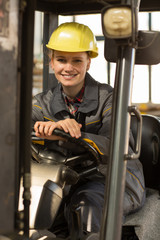 Female industrial worker sitting on forklift truck, looking and smiling at camera.