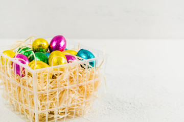 Colorful Easter chocolate eggs in basket with hay on white background