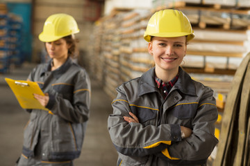 Female warehouse worker with arm crossed in front background of shelves.