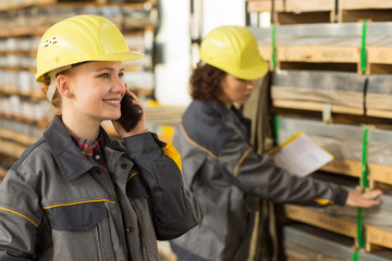 Female worker speaking on mobile phone while her colleague checking shelves.