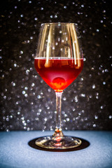 A glass of red wine, the background is black sparkling, the tank is illuminated with a directional light from above