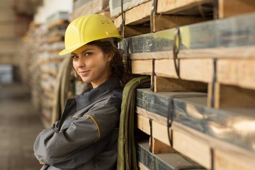 Smiling female brunette worker in warehouse leaning by back on shelf and posing at camera with...