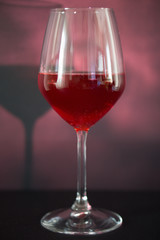 A glass of red wine, the background is reddish, the tank is illuminated with diffused light from the side