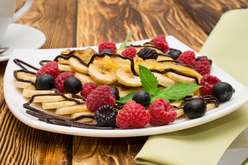 Homemade crepes served with chocolate cream, Banana, fresh blueberries, raspberries on a wooden background, pancakes