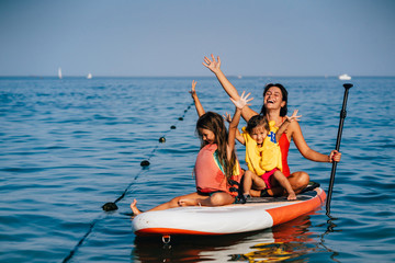 Mother with two daughters stand up on a paddle board