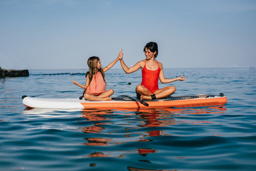 Mom and little daughter doing yoga on the paddle board
