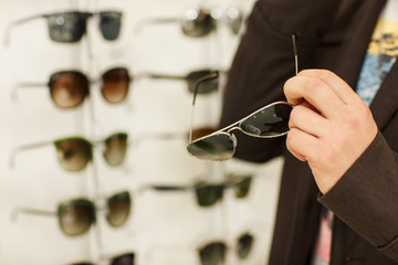 Cropped close up shot of a male customer holding sunglasses, while shopping at the optician store....