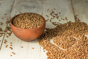 Dry buckwheat in brown clay bowl on wooden table. gluten free grain for healthy diet