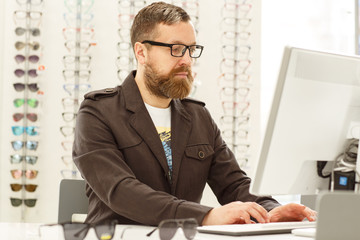 Horizontal shot of a mature professional male optometrist working on a computer at his eyewear...