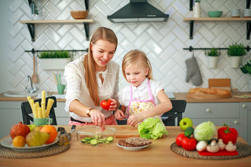 Mother with her daughter in kitchen preparing healthy food with fresh vegetables