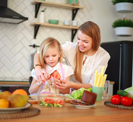 Mother with her daughter in kitchen preparing healthy food with fresh vegetables