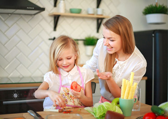 Mother with her daughter in kitchen preparing healthy food with fresh vegetables
