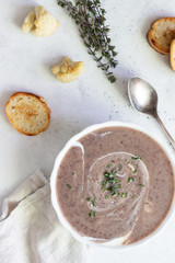 Cream soup with cauliflower and red bean served with sour cream and thyme. Light grey concrete background. Copy space. Comfort food.