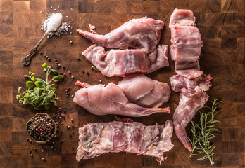 Top of view portioned rabbit legs and saddle with herbs and spices on butcher board
