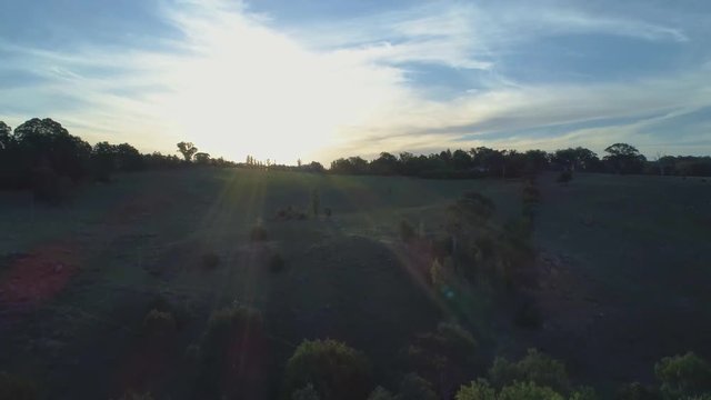 Slow rise over countryside and meadows facing the sun with flare