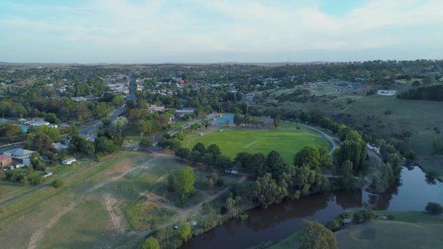 Backward flight over river away from small town houses at sunset in Australia