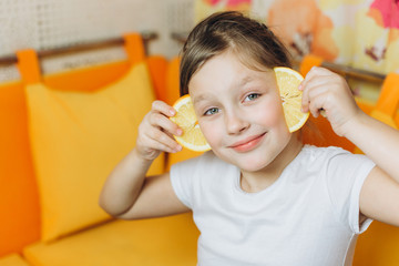 Cheerful nice pretty happy girl playing, joking with fresh orange at home in the kitchen. Childhood, healthy, positive, colorful concept