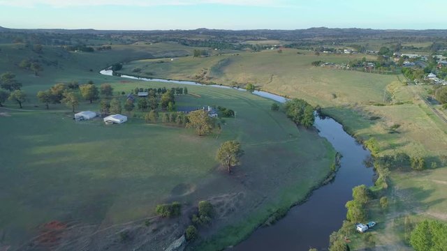 Forward flight over green grassy hills and winding creek at sunset